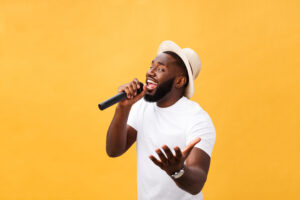 young handsome african american boy singing emotional with microphone isolated on yellow background, in motion gesturing