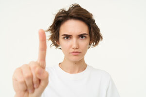 Close up of serious young woman shows one finger, stop, taboo gesture, disapprove something, blocking, saying one rule, standing over white background