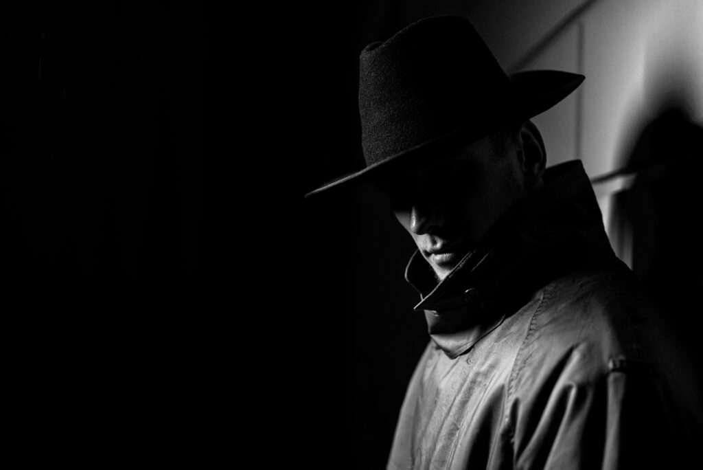 dark portrait of a man in a raincoat with a hat at night on the street