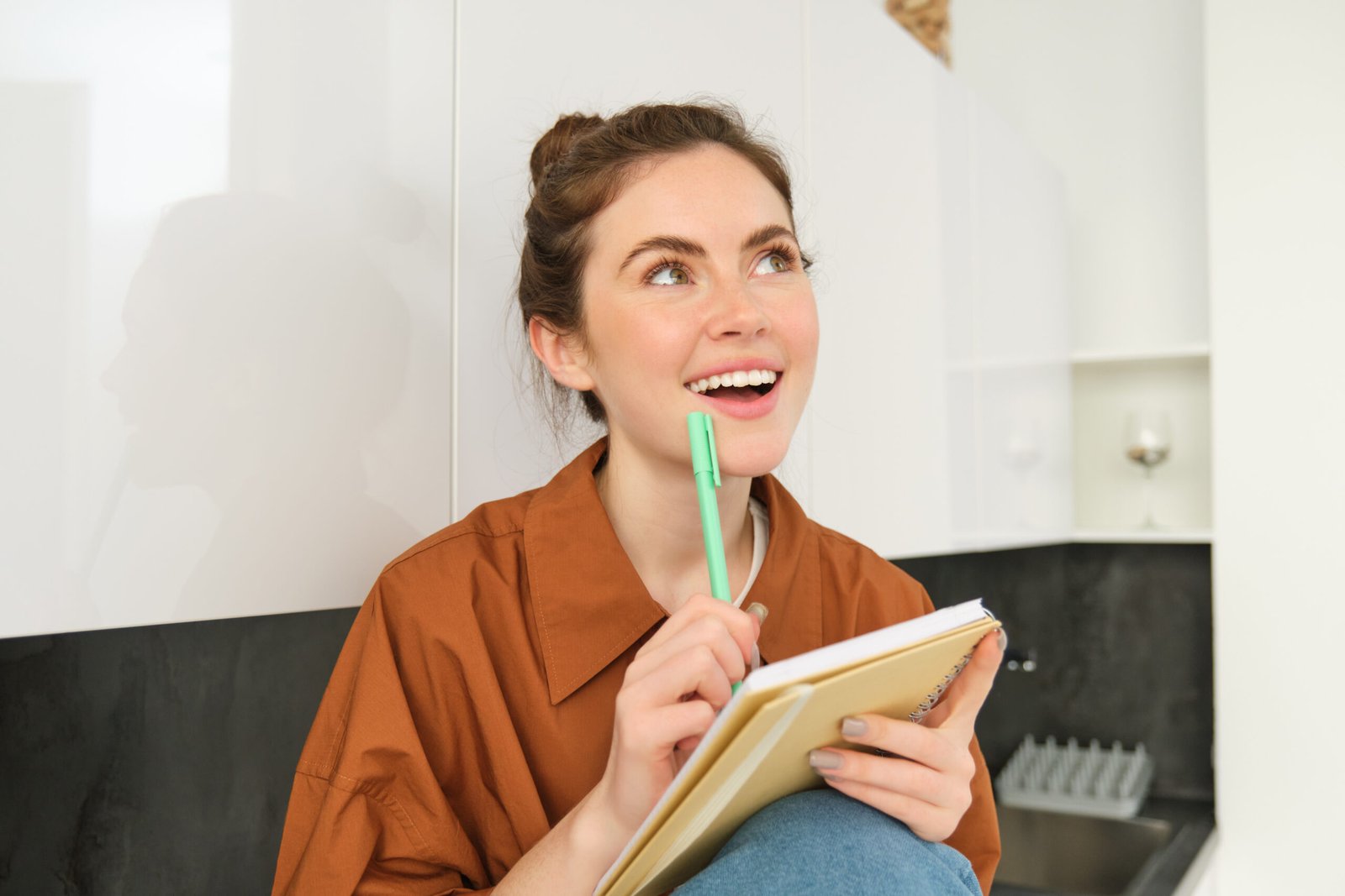 Portrait of young smiling woman with creative thoughts, looking up with inspired face, holding pen and notebook, writing down her ideas registro de marcas e patentes